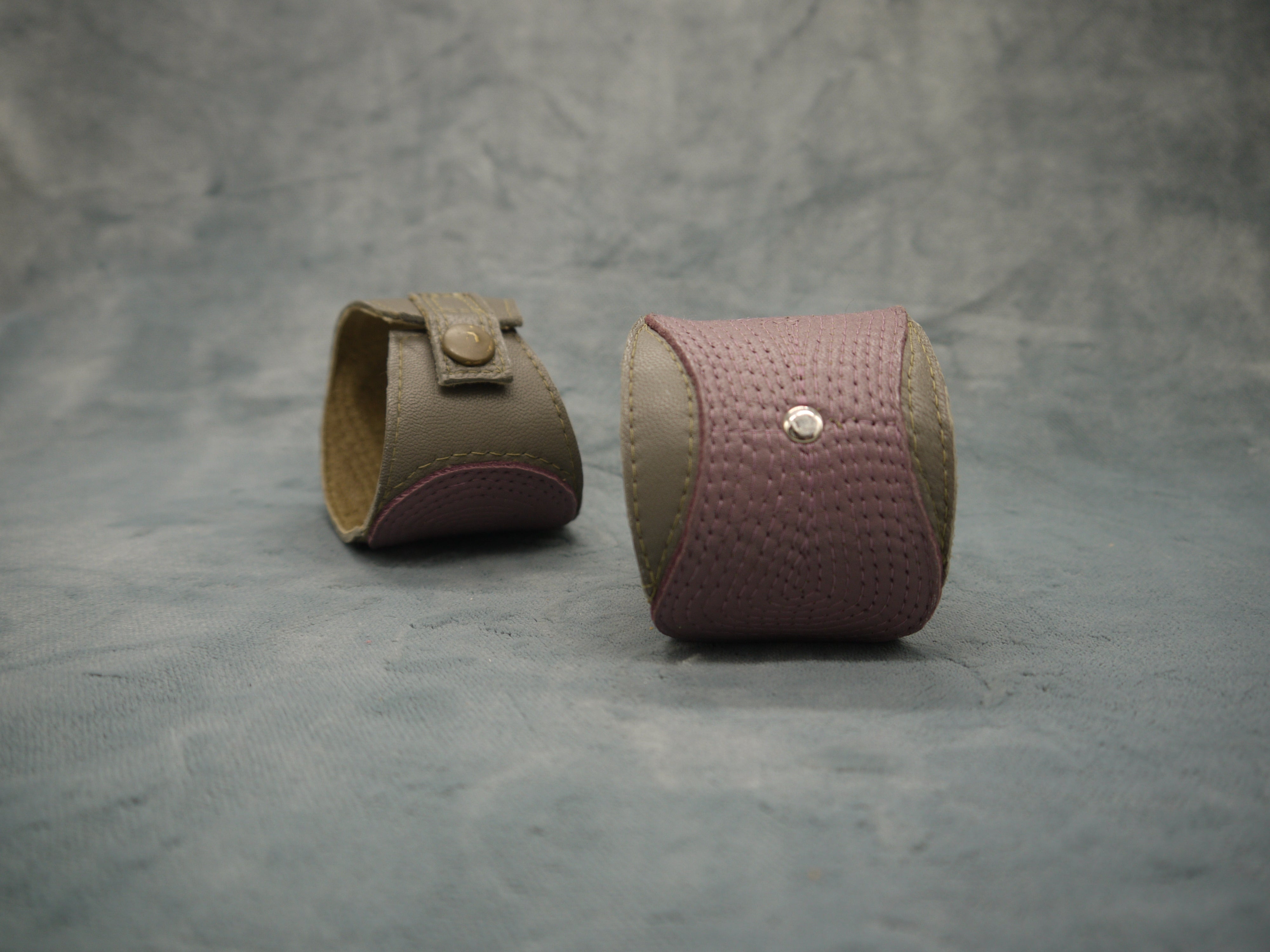 Leather cuff in olive green and smokey lilac. The central smokey lilac lozenge shape section has a concentrical stitching detail.There is a central steel circle as a focal point where the stitching ends. Twi cuffs are shown in the image