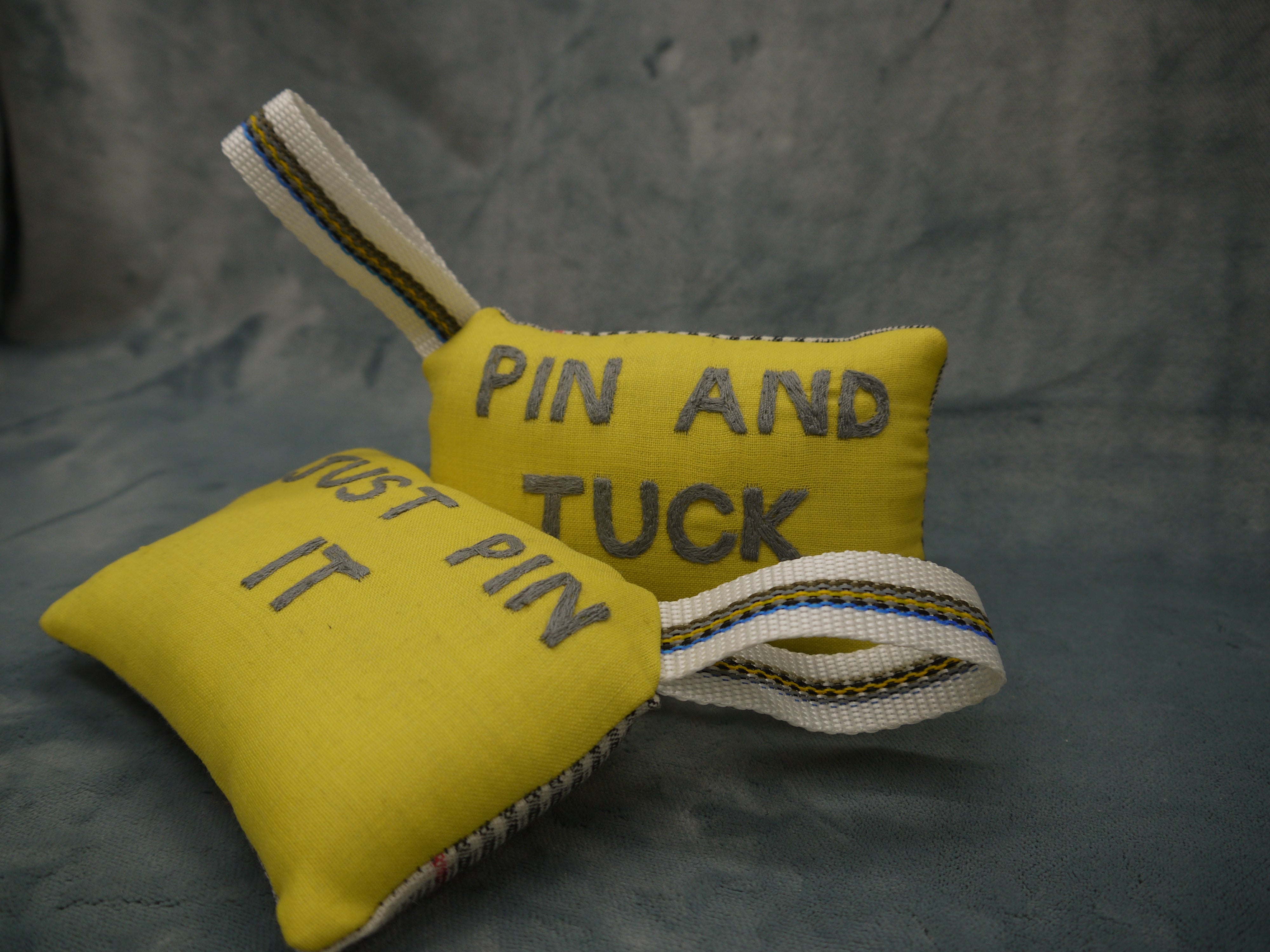 Pin cushion in yellow and grey wool, superfine 120, Pin and Tuck Embroidered by hand in grey on a yellow background, Nylon wriststrap with yellow/blue go stripe, Prince of Wales wool backing in white and black