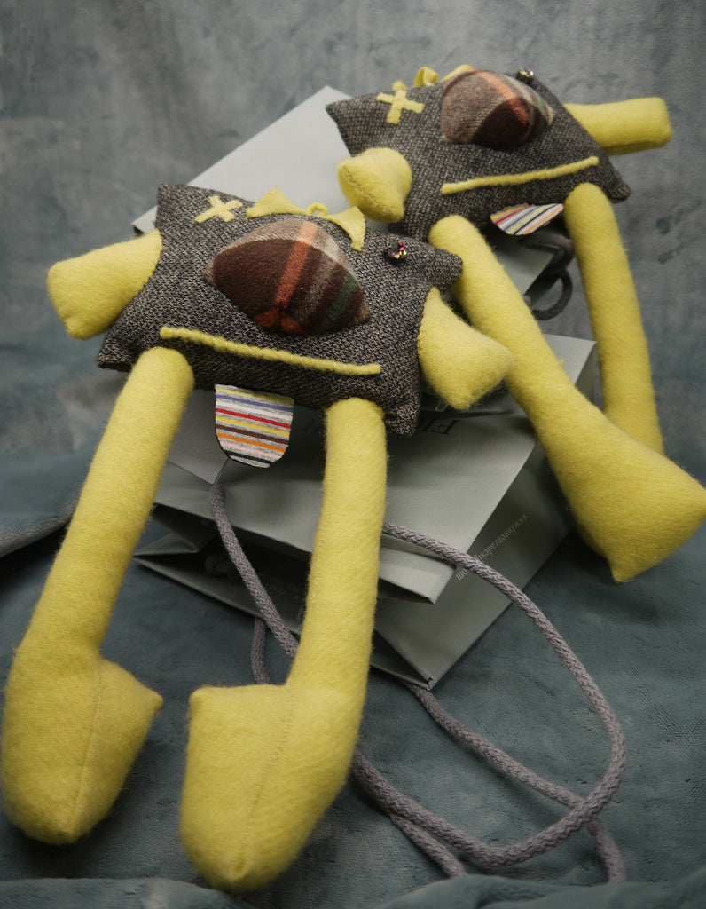 Squaru Stuffed Monster toy designed and produced by Godi Fiorenza, made in Italy, in brown melange cashmere suiting and soft yellow brushed cashmere. The square body of the Monster Toy is in brown cashmere with a checked pattern large nose. The short arms and extra long legs are in  yellow cashmere. One eye is a hand yellow cashmere cross the other is a brown/green crystal. The tongue is in thin stripes, multicoloured jersey