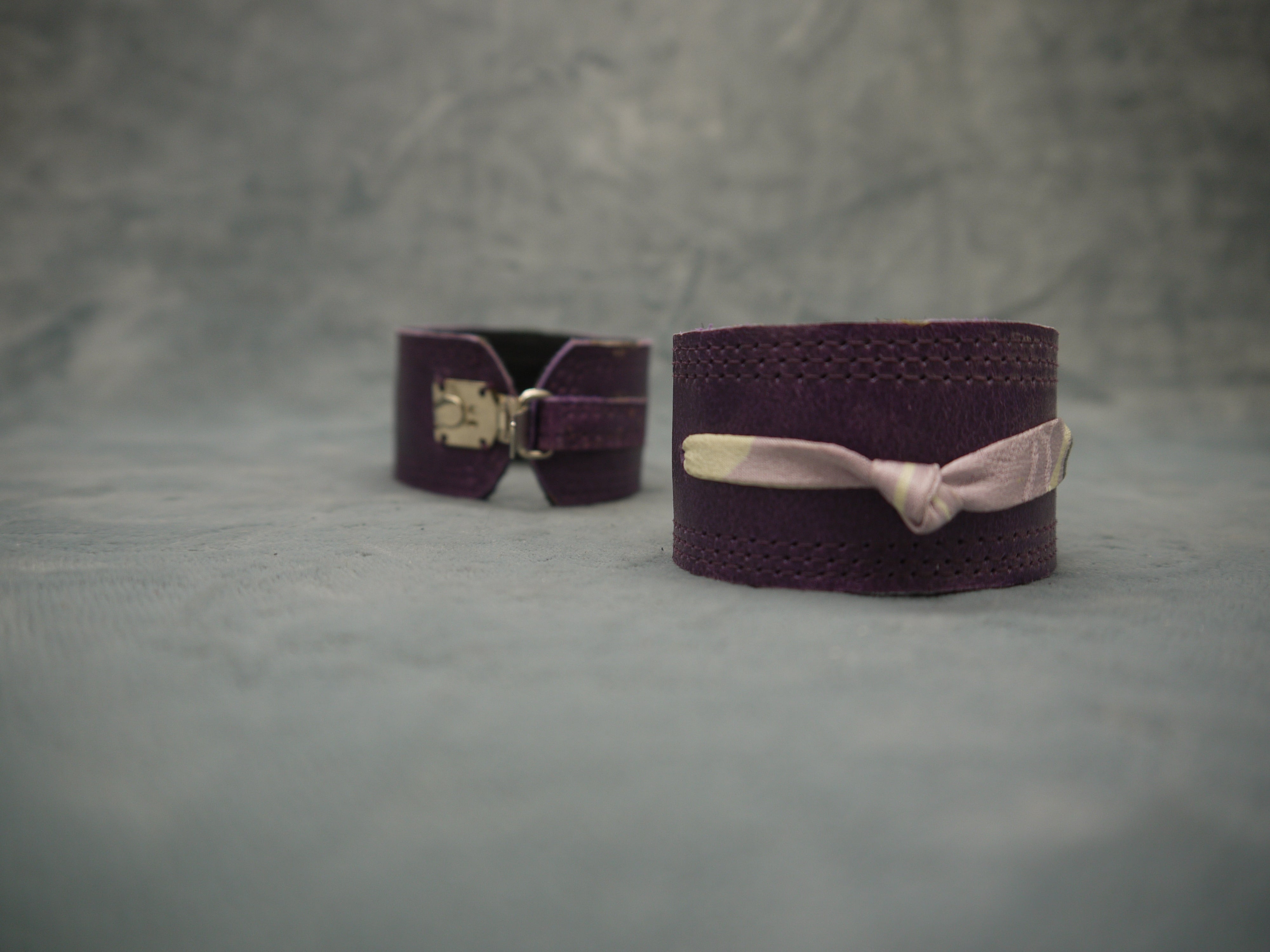 Royal Purple slimline Italian leather cuff with lilac slim silk knot central on the cuff. The cugff has elegant repeat stitch detail around the edges. Close-Up Image. Two cuffs are shown worn, one from the front and one from the back with the clasp closure .