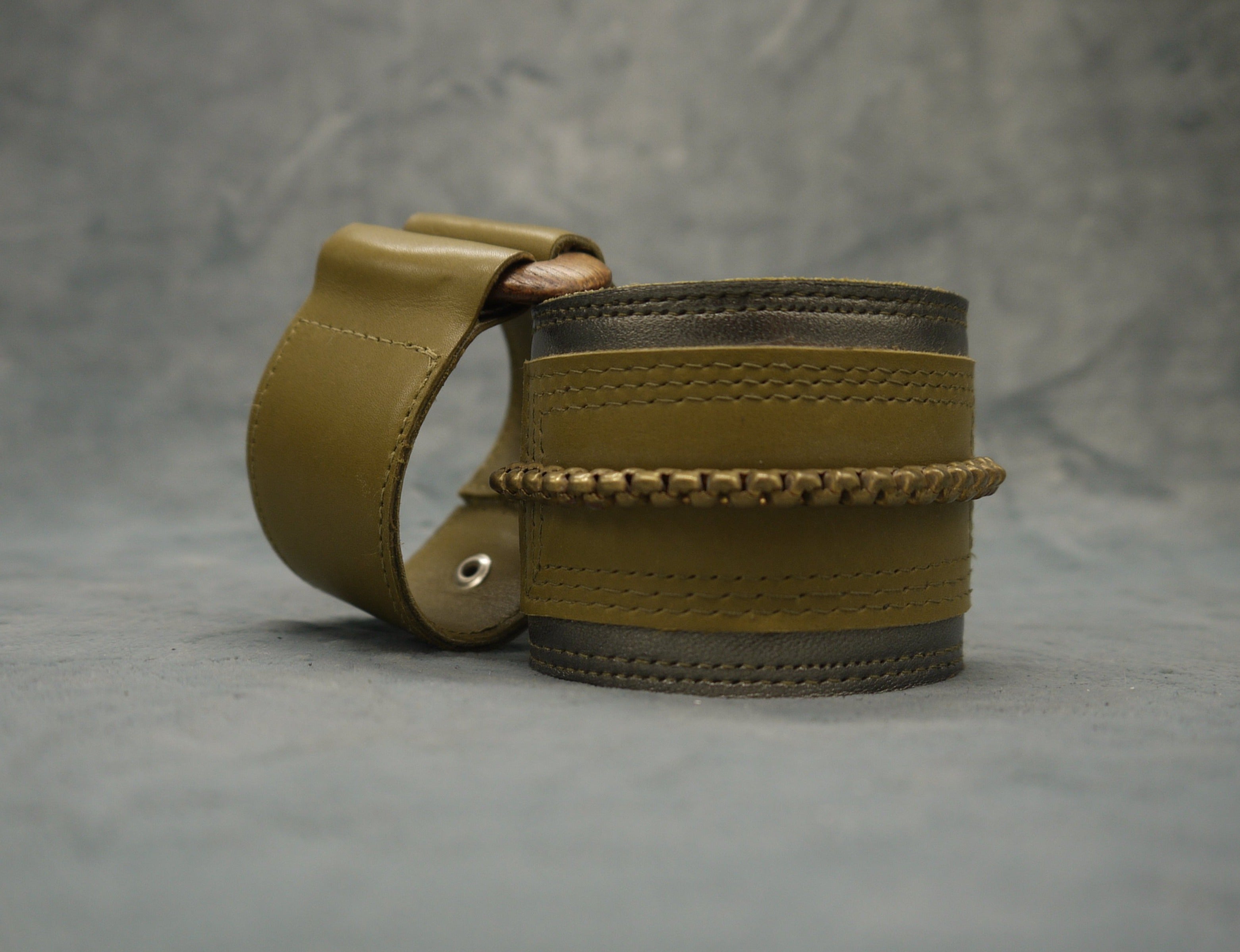 Leather cuff in Gunmetal metallic leather and moss green leather central rectangle which has repeat stich detail which frames the rectangle. A central brass chain is the focal point of the cuff, sewn central across the moss green rectangle.