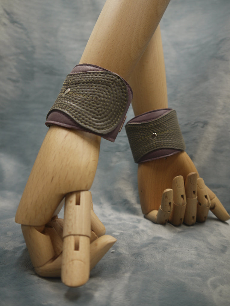 Leather cuff  in olive green and smokey lilac. The central olive lozenge shape section has a concentrical stitching detail.There is a central steel circle as a focal point where the stitching ends.
