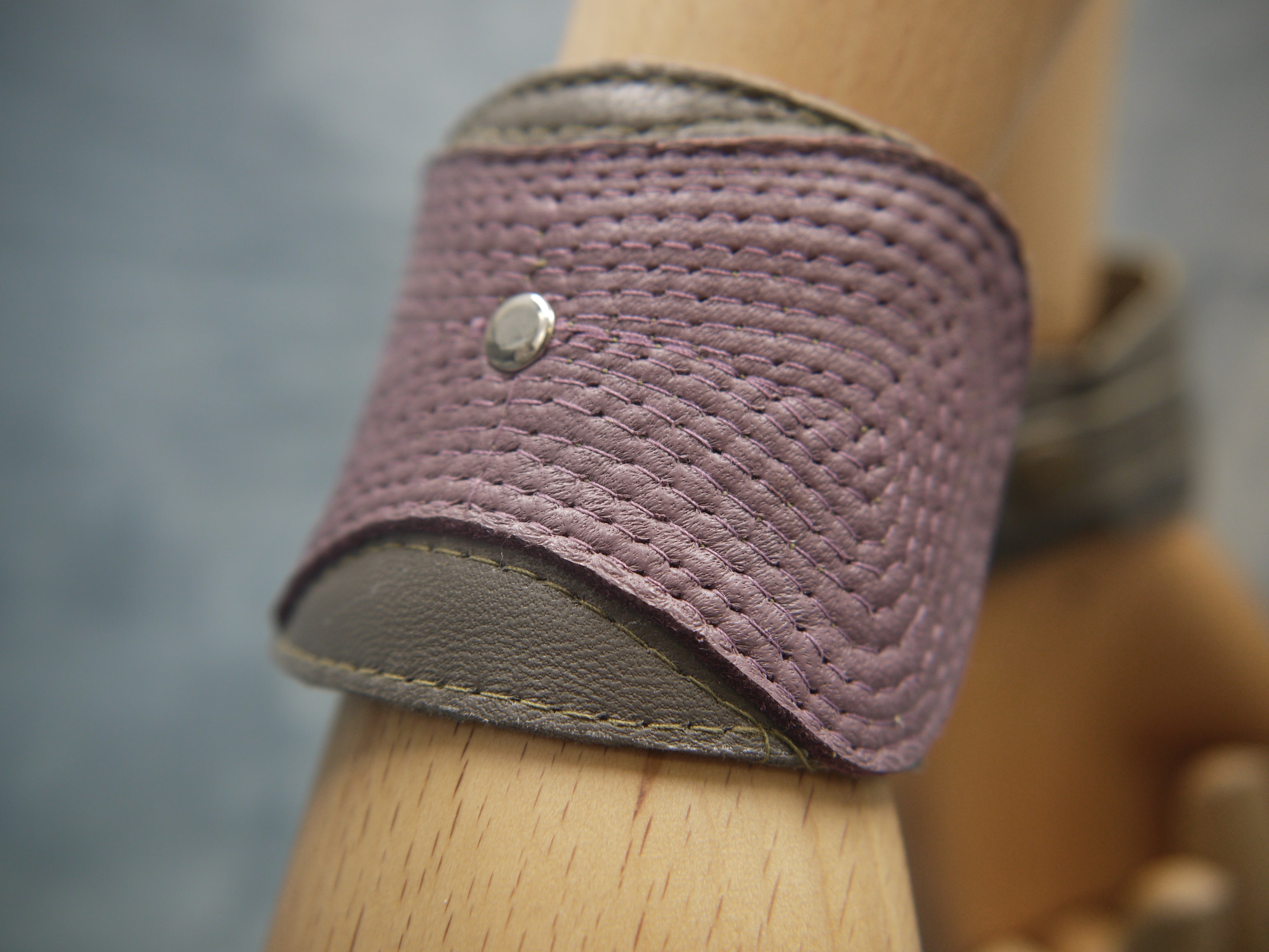 Leather cuff in olive green and smokey lilac. The central smokey lilac lozenge shape section has a concentrical stitching detail.There is a central steel circle as a focal point where the stitching ends. Close-Up image