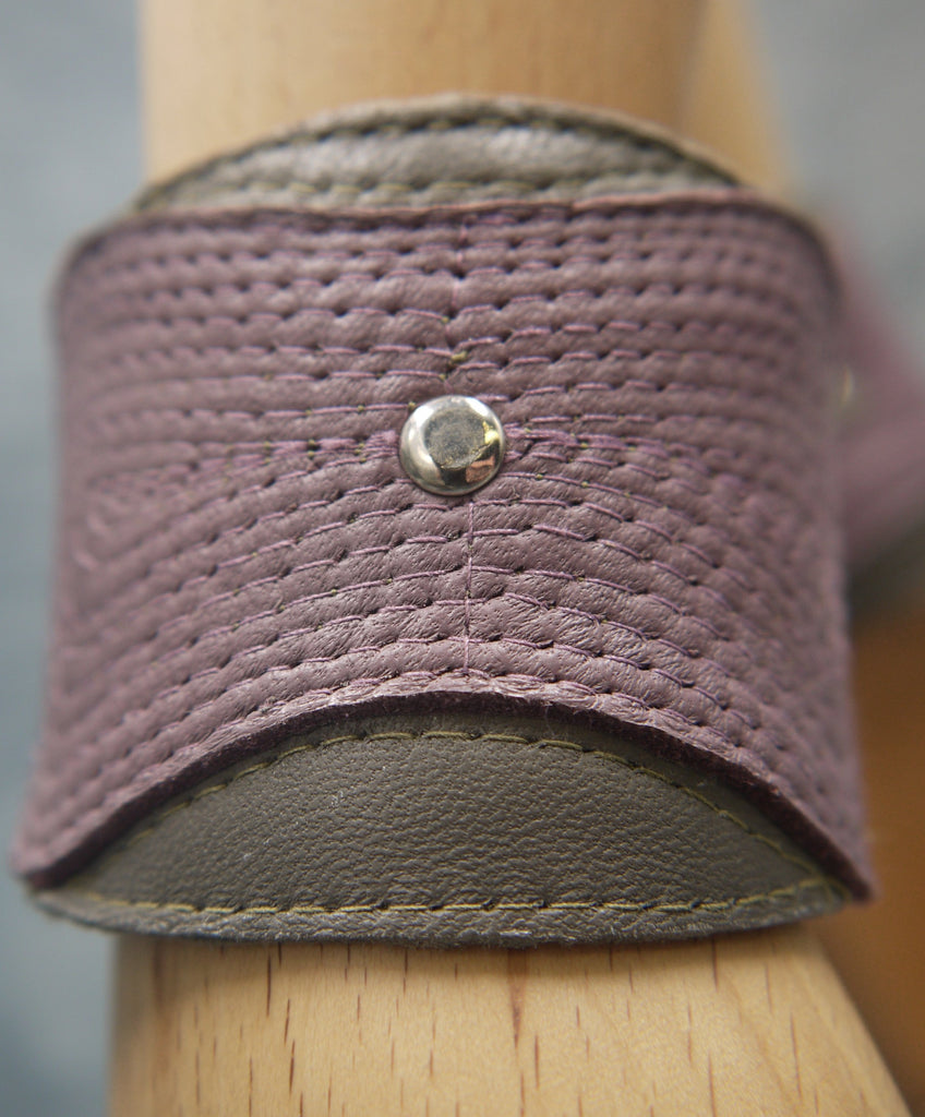 Leather cuff in olive green and smokey lilac. The central smokey lilac lozenge shape section has a concentrical stitching detail.There is a central steel circle as a focal point where the stitching ends. Close-Up Image