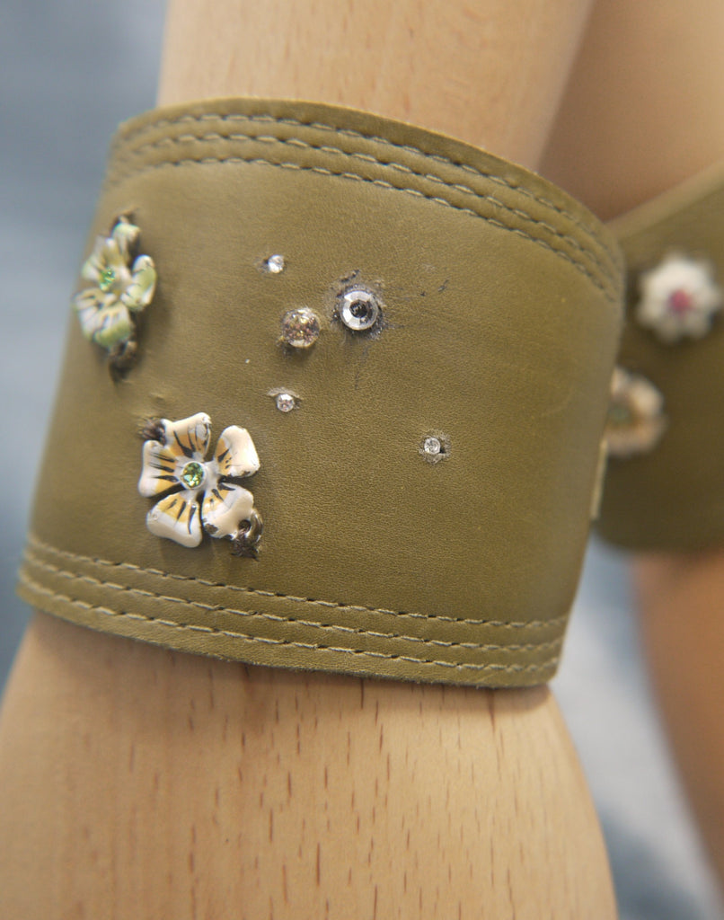 Leather Cuff in Moss green nappa, with repeat stitch edge detail . Set with two enamelled flowers on pale apricot and pale green. Also set with clear crystals which create a dew drop effect