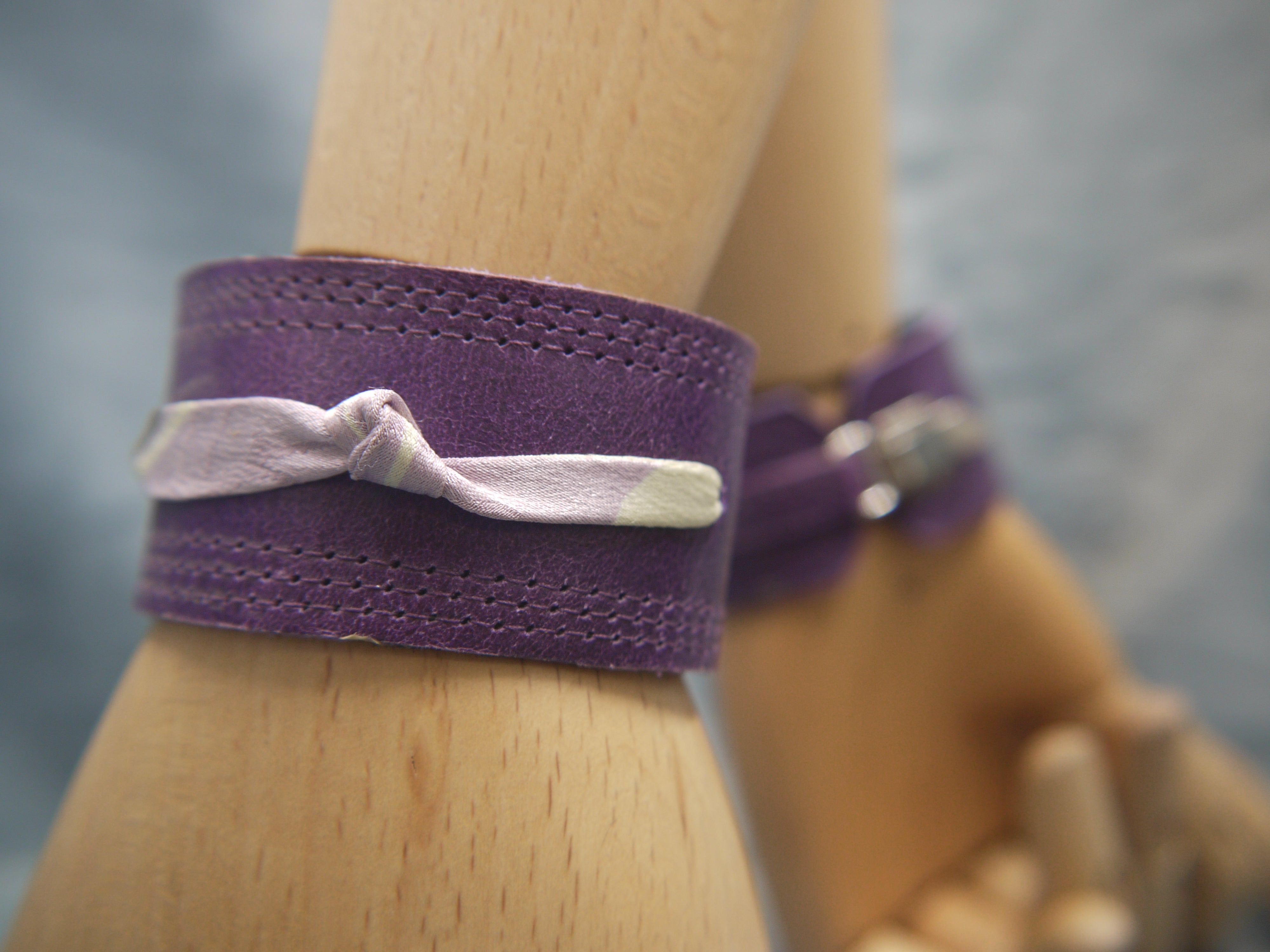 Royal Purple slimline Italian leather cuff with lilac slim silk knot central on the cuff. The cugff has elegant repeat stitch detail around the edges. Close-Up Image. Two cuffs are shown worn, one from the front and one from the back with the clasp closure .