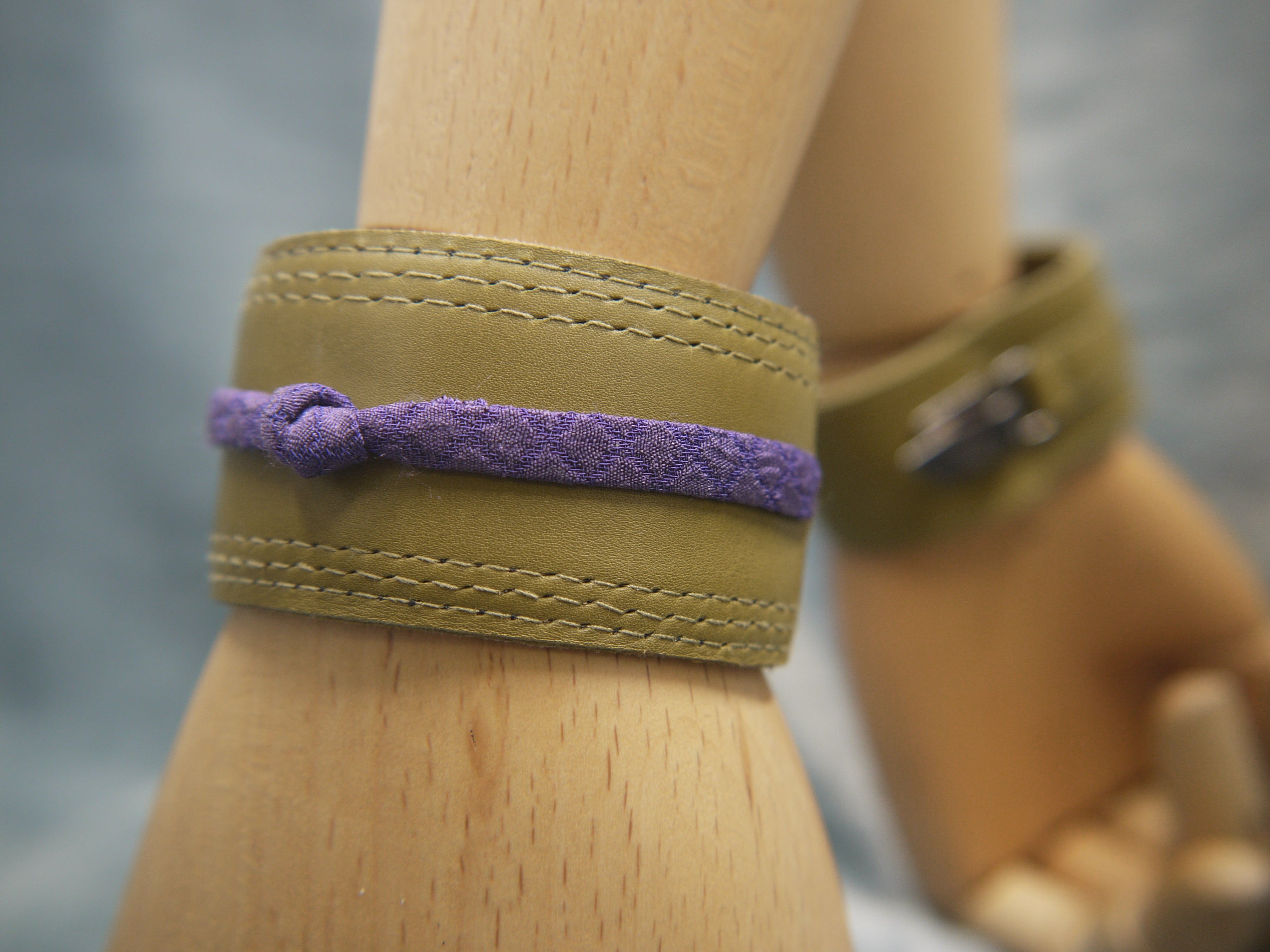 Olive green slimline Italian leather cuff with royal purple slim silk knot central on the cuff. The cugff has elegant repeat stitch detail around the edges. Close-Up Image. Two cuffs are shown. One front view, one back.