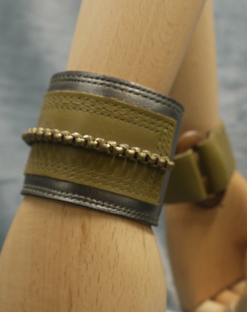 Leather cuff in Gunmetal metallic leather and moss green leather central rectangle which has repeat stich detail which frames the rectangle. A central brass chain is the focal point of the cuff, sewn central across the moss green rectangle.