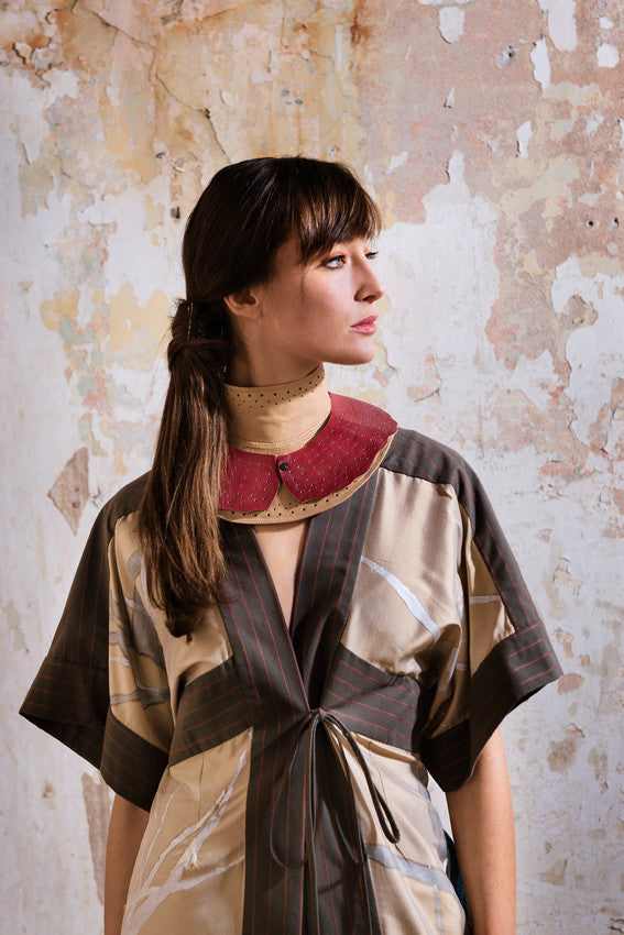 Model wearing beige high neck punchwork collar  with red leather Peter Pan collar worn over  the top. Model also wears handpainted shirt kimono in beige golden silk with repeat white winter tress pattern